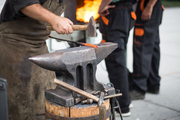 The blacksmith manually forging the molten metal on the anvil in smithy with spark fireworks