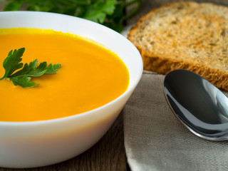 white bowl of pumpkin soup decorated with parsley greens, on the background of wooden old table.