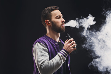 Young man vaping e-cigarette with smoke on black