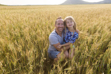 portrait of a father and daughter playing in the wheat field at sunset.