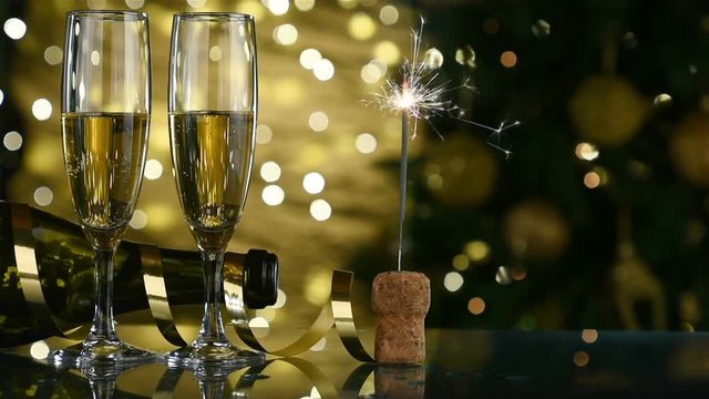 Champagne flutes, sparks on cork, Christmas tree light background