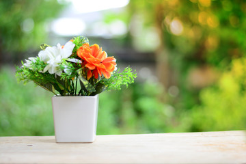 a white vase with white and orange  flowers  on wooden table  with orange light in morning