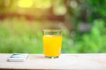 a glass of orange juice  and white mobliephone on wooden table in garden