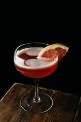 Pink cocktail garnished with a slice of blood orange on dark background