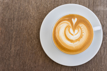 A white cup of coffee latte art on wood table