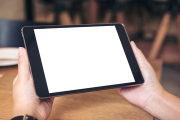Mockup image of hands holding black tablet pc with blank white screen with coffee cup on wooden table in cafe