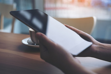 Closeup image of a woman holding and using tablet pc with coffee cup in modern cafe