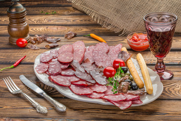 Meat appetizer selection. Salami, prosciutto, bread sticks, olives and sun-dried tomatoes, one glasse red wine over wooden background