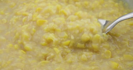 Close video of slowly stirring cream style corn with a large metal spoon in a skillet while heating. - Powered by Adobe