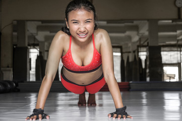 Fototapeta na wymiar sexy sweaty Asian woman in sport clothes doing push ups on gym dojo floor smiling in hard training fitness workout