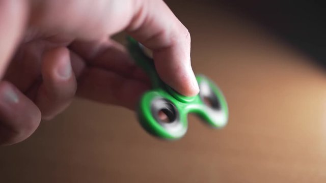 Man twists green spinner in his hand, fidget spinner is twisting round and round