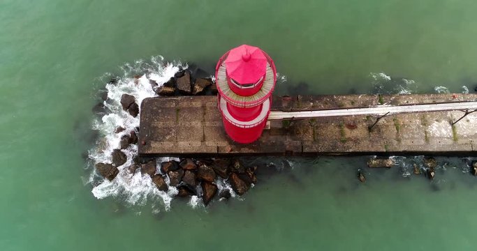 Looking down on red lighthouse in turbulent waters on windy Autumn day. This footage is running in reverse which gives the breaking waves a surreal quality.