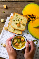 Cup with carrot cream soup in girl hands with seeds, crackers on wooden rustic background, copy space for your text