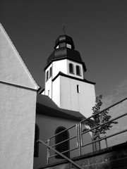 Schneeweißer Kirchturm der katholischen Pfarrkirche St. Johannes Baptist bei Sonnenschein in Schloß Holte-Stukenbrock bei Gütersloh in Ostwestfalen-Lippe, fotografiert in traditionellem Schwarzweiß