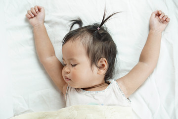 Cute toddler girl sleeping on white bed sheets cuddle in yellow blanket, bright room