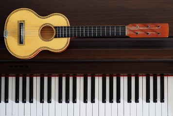 Obraz na płótnie Canvas Old ukulele next to a piano keyboard