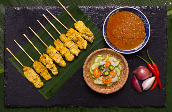 Pork satay skewer with peanut sauce decorated with cucumber sauce, onion, chili on banana leaf.