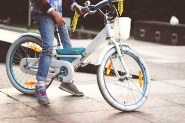 Fototapeta premium A little girl in ragged jeans sits on a small white white bicycle with white wheels in the park