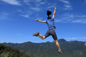 successful woman hiker jumping on mountain top