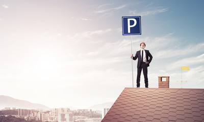 Young businessman with parking sign standing on brick roof. Mixe