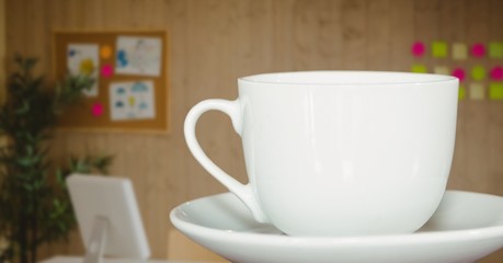 White coffee cup on saucer against blurry office with dark