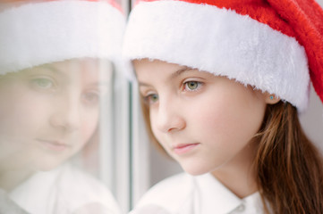 beautiful little girl in Santa hat dreaming by the window