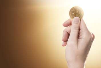 Hand holding a golden Bitcoin on a gently lit background with copy space. 3D rendering