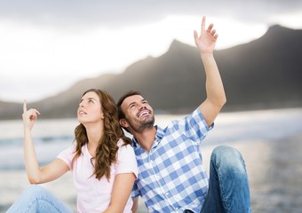 Couple sitting and pointing against blurry beach