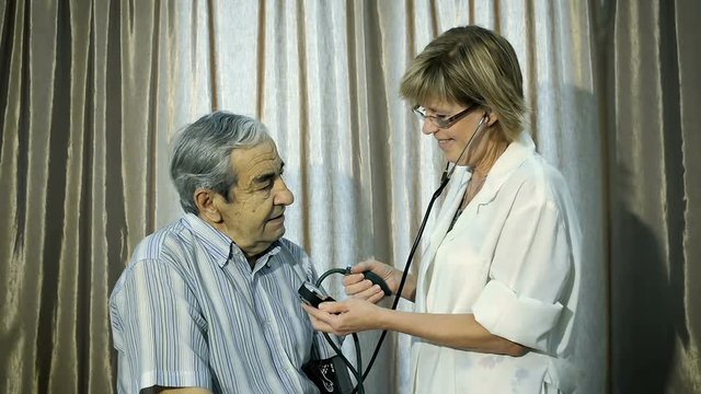 Cheerful nurse checks the blood pressure of an elderly man of seventy years.