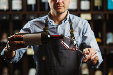 Male sommelier pouring red wine into long-stemmed wineglasses.