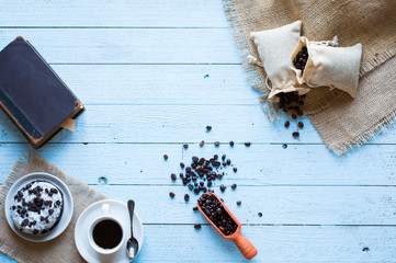 Coffee beans and cup of coffee with other components on different wooden background.