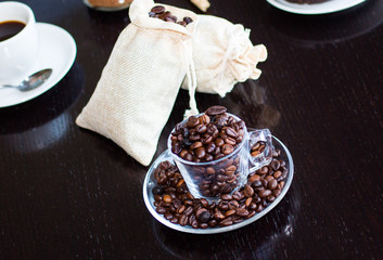 Coffee beans and cup of coffee with other components on different wooden background.