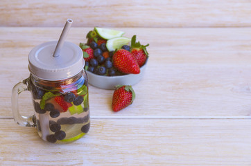 Detox infused water with lime, strawberries, blueberries and mint in mason jar on wooden background. Cleansing drink to lose weight. Healthy lifestyle, detox diet concept.