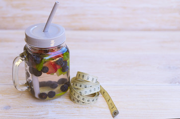 Detox infused water with lime, strawberries, blueberries and mint in mason jar with centimeter on wooden background. Cleansing drink to lose weight. Healthy lifestyle, detox diet concept.
