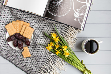 Cup of coffee, cracker biscuit cookies, date fruits, book with bicycle and daffodil flowers. Top view, flat lay