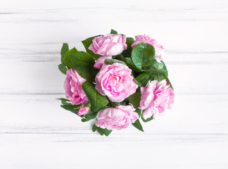 Rose flowers in a vase against white vintage wooden table. Flat lay, top view