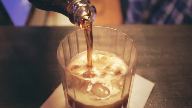 Pouring cola in glass with ice. Whisky glass. Whisky cola. Whiskey liquid. Close up of whiskey ice cola drink. Pouring coca cola from bottle into glass with ice cubes