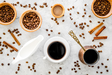 Cup of black coffee near coffee beans, milk and cinnamon on grey background top view