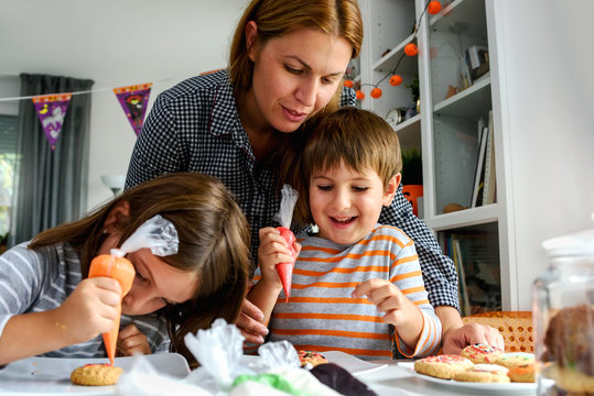 Mother With Kids Decorating Cookies For Halloween