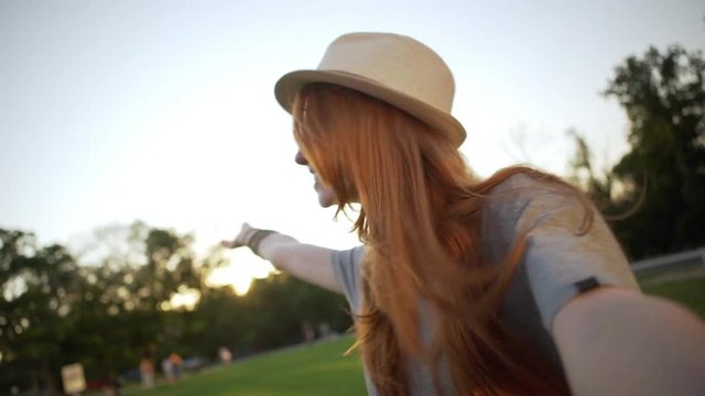 happy smiling girl with red long hair taking selfie video inviting friends to join her in nice park slomo closeup