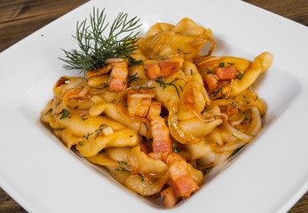 Dumplings with potatoes and bacon in a bowl on a wooden table.