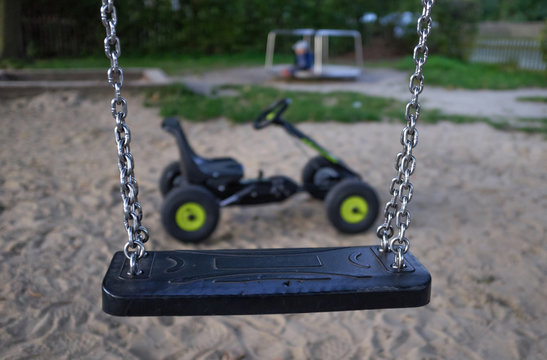 Eine Kinderschaukel mit einem Tretauto und Spielplatz im Hintergrund
