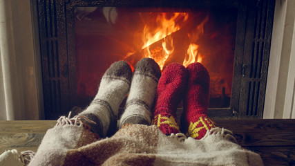 Toned photo of couple feet wearing warm socks lying under blanket by the burning fireplace
