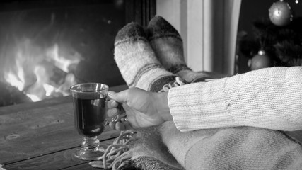 Black and white closeup image of young woman holding cup of tea at burning fireplace