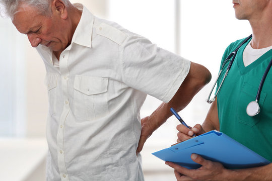 Doctor and senior male patient suffering from back pain during medical exam.