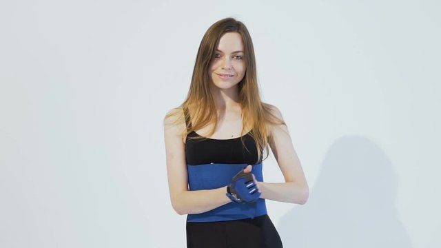 Dark hair girl, wearing a black top and leggins, is putting on a blue belt around her back in the white background, isolated, slow motion