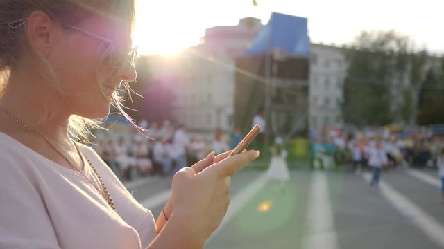 happy female holds android standing at downtown, women sitting on mobile Internet Outdoors, young woman with smartphone into hands on street, smiling girl with cell phone in arm outside,