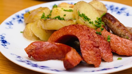 Roasted sausages served as diner on blue and white plate. Potatoes speinkled with chopped chives as sidedish