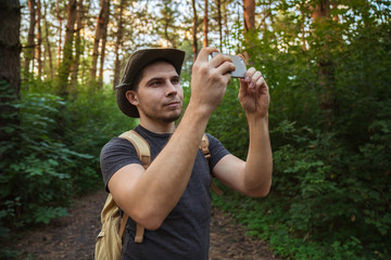 Man in the forest makes the photo on the phone.