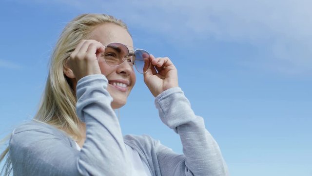 Sweet Young Blonde Runs Hand Through Her Beautiful Blonde Hair and Put's on Aviator Sunglasses. She Looks Far Away into the Bright Clear Sky and Cloudless Future. 